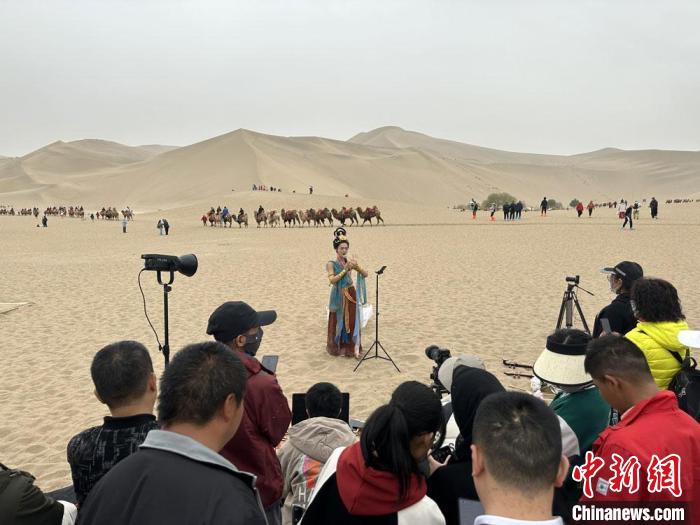 圖為2023年4月底，敦煌大漠“逐舞者”奧楠在鳴沙山月牙泉景區(qū)視頻直播，吸引游人圍觀?！●T志軍 攝